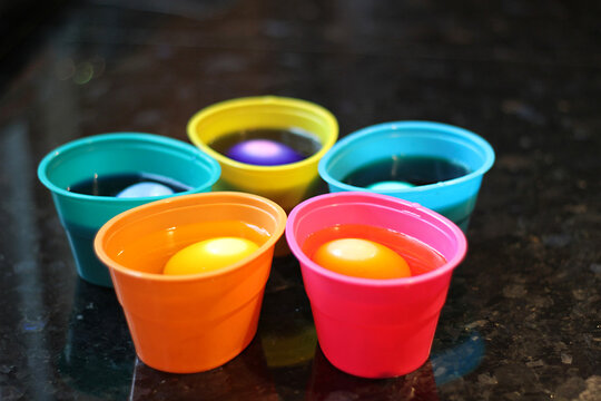 5 cups of eggs sitting in dye at Easter time