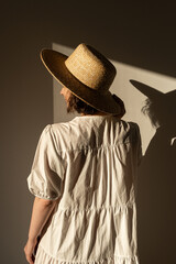Young pretty woman in straw hat and white dress / sundress. Sunlight shadow on the wall. Minimal...