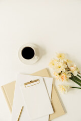 Beautiful modern office workspace with clipboard and stationery and narcissus flowers. Flatlay, top view minimalist work table. Blank sheet paper with mockup copy space