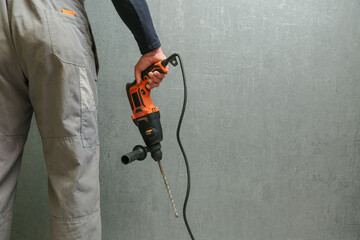man's hand holds hammer drill on the background of gray wall with copy space