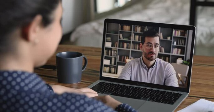 Job interview by videocall, hiring concept. Due corona virus or covid-19 businesspeople negotiate remotely use video conference app, laptop screen view over girl shoulder sit at desk talk by videocall