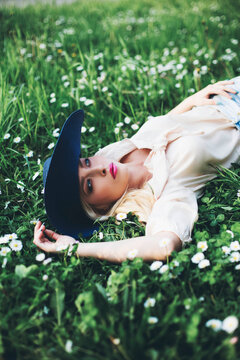 Beautiful young woman lying on grass wearing a summer hat