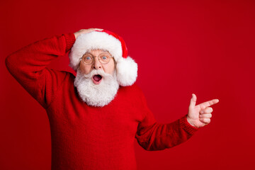 Photo of amazed grey hair old man in santa claus hat point index finger copyspace impressed jolly holly x-mas ads promo wear sweater isolated over bright shine color background