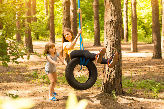 Happy child daughter pushing mother on tire swing in garden