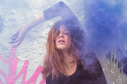 Young woman and purple smoke in front of graffiti wall