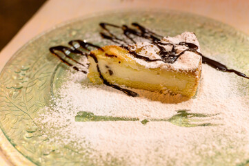Piece of cheese cake with chocolate sauce and white sugar powder