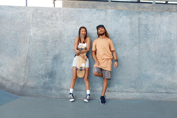 Skaters. Girl And Guy At Skatepark. Portrait Of Hipster Couple In Casual Outfit With Skateboard Against Concrete Wall At Park. Urban Subculture Style And Summer Sport In City. Active Lifestyle. © puhhha