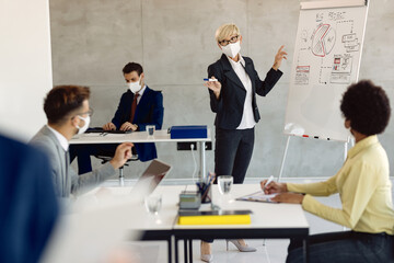 Mature businesswoman wearing face mask while giving presentation to her colleagues in the office.