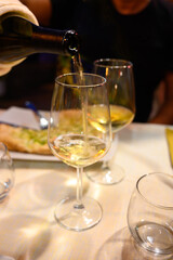 Pouring in glass  cold dry white wine in outdoor cafe at night in Italy
