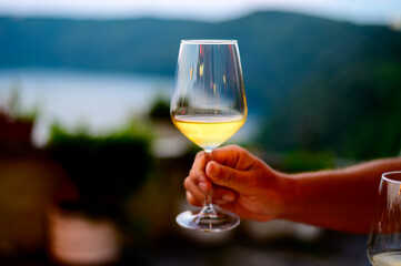 Hand with glass of cold dry white wine served outdoor in cafe at night in Italy