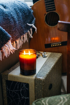 candle burning on guitar amp with acoustic guitar and blanket in background
