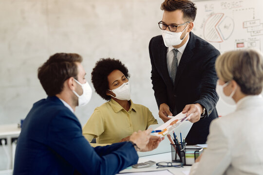 Group of business colleagues with face masks analyzing graphs on a meeting in the office.