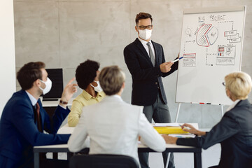 Male entrepreneur with face mask giving business presentation to his coworker in the office.