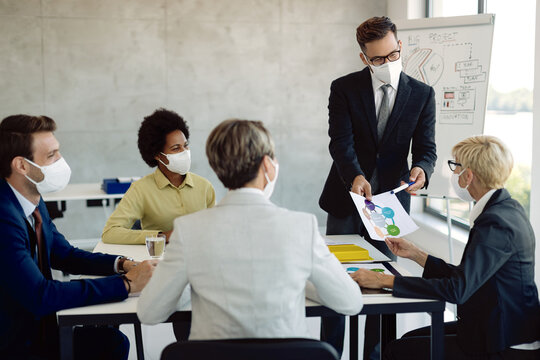 Group of business people with face masks examining graphs on a meeting in the office.