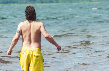 Fototapeta na wymiar View from behind of a man with long hair and a yellow vintage bathing suit, coming into the sea.