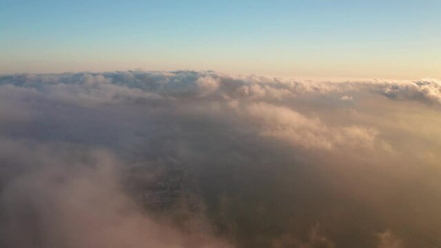 Aerial video over low clouds and morning fog hovering over a sea coastline at sunrise