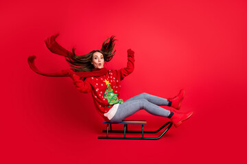 Full length body size profile side view of her she attractive cheerful cheery amazed girl sitting on sledge having fun riding season leisure isolated bright vivid shine vibrant red color background - obrazy, fototapety, plakaty