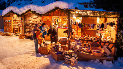 Naklejka na ściany i meble Romantic Christmas market with illuminated shops in wooden huts with gifts and handmade decoration.