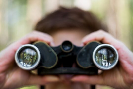 Person holding binoculars with forest reflection on the front element