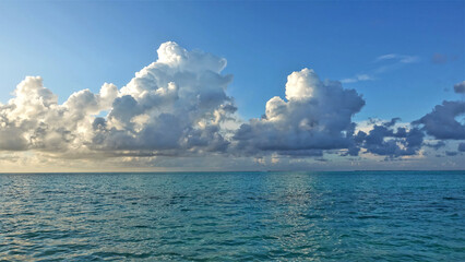 Obraz premium The white clouds over the Indian Ocean are illuminated by the sun. The aquamarine water is calm. Summer day, blue sky. Maldives. Male