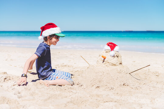 Boy smiling at a sand snowman at the beach at Christmas in Australia