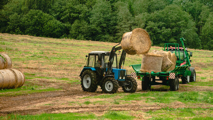tractor loads round bales of straw on the trailer
