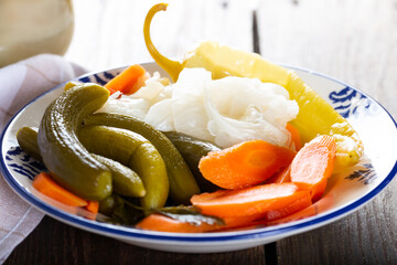 Assorted pickled vegetables in bowl/plate with garlic and salt in bowl on natural wooden background.