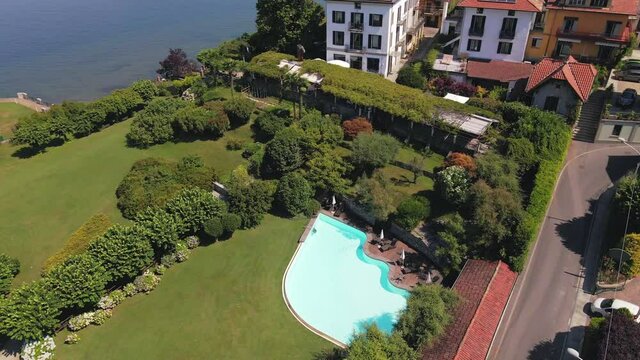 Drone view of turquoise swimming pool in green garden revealing blue Lake Maggiore
