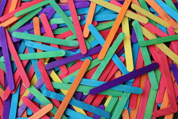 Fototapeta na wymiar Multicolored popsicle sticks in bulk in shades of purple red light blue yellow orange green for desktop background c