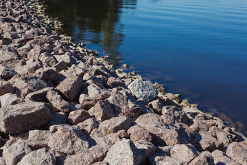 Stone embankment, lots of bulky granite stones on a lake shore