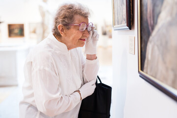 mature woman  examines paintings in an exhibition in hall of an art museum