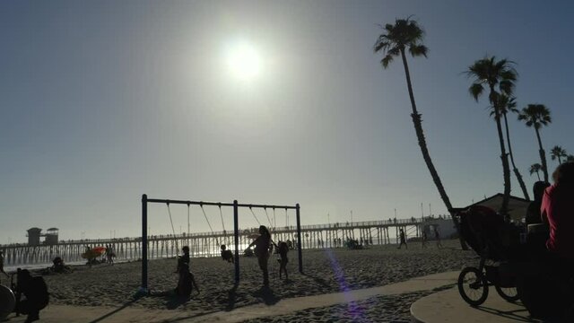 Kids playing on the swings at the Oceanside beach, pregnant mother standing by.