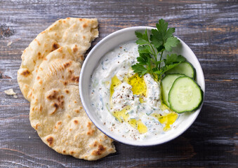 Traditional greek yogurt tzatziki sauce with cucumbers and herbs on wooden background, space, top view