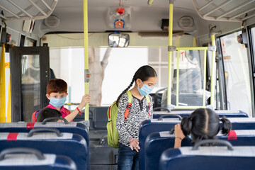 Kids with medical mask coming inside school bus and sitting on seats while maintaining social...