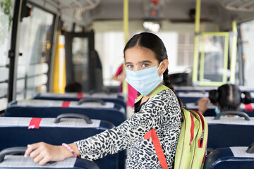 Portrait of Girl kid student in medical mask inside the school bus looking at camera - Concept of school reopen or back to school with new normal lifestyle