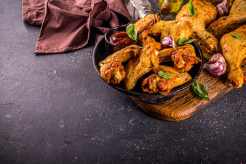 Grilled chicken legs and wings, with herbs, spices, garlic and barbeque sauce, dark concrete table background copy space top view