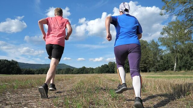 Guy and girl running on the harvested field. Sports healthy lifestyle. Running athletes enjoy run together. Slow motion