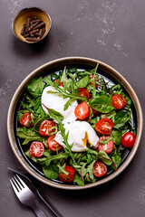 Cherry Tomatoes, poached eggs and herbs mix salad on dark background. Simple and healthy nutrition. Selective focus