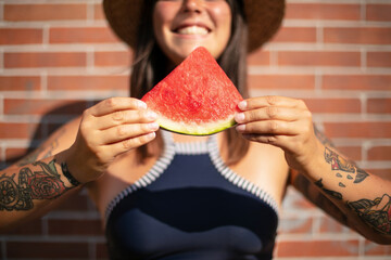 Young smiling woman with tattoo eats watermelon in the summer