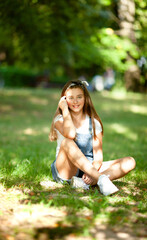 Naklejka na ściany i meble teenager girl in denim overalls sits on the grass, lit by sun bunnies