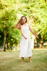 beautiful girl in a light white dress with polka dots is spinning in the park on the grass