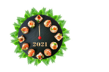 Happy New Year 2021! Smoked salmon canapes on black slate platter form a clock face showing midnight over a fir tree wreath isolated