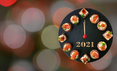 Happy New Year 2021! Smoked salmon canapes on black slate platter form a clock face showing midnight over bokeh background