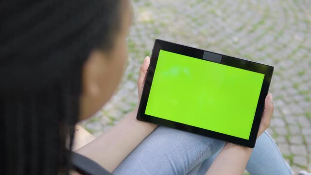 A black woman looks at a tablet with green screen - horizontal position - focused closeup from behind