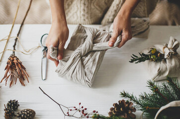 Plastic free holidays, zero waste Christmas. Hands wrapping christmas gift in linen fabric in...