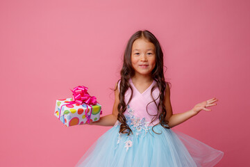 a little girl of Asian appearance holds a gift in her hands celebrating her birthday on a pink background