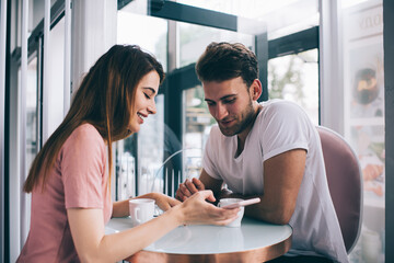 Happy couple using smartphone while sitting in cafe in daytime