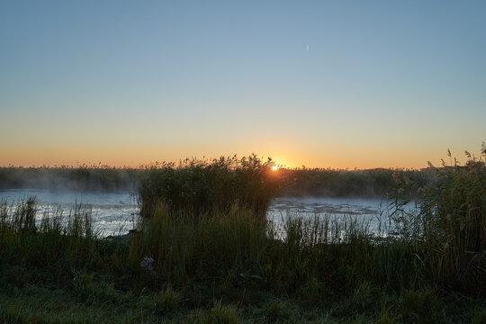 Autumn time. Dawn over the river in a misty, brooding haze. Beautiful view of the forest and river, covered with fog in the early morning. The sun's rays of light. September.