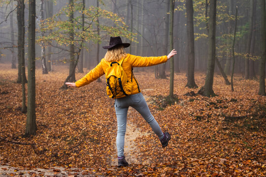 Hiking in autumn forest. Woman tourist with cowboy hat and backpack walking at footpath