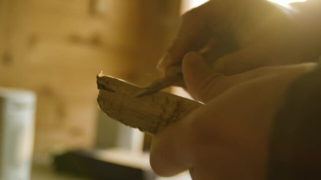 Male hand carving into a piece of wood close up while the sun shines through the window	
